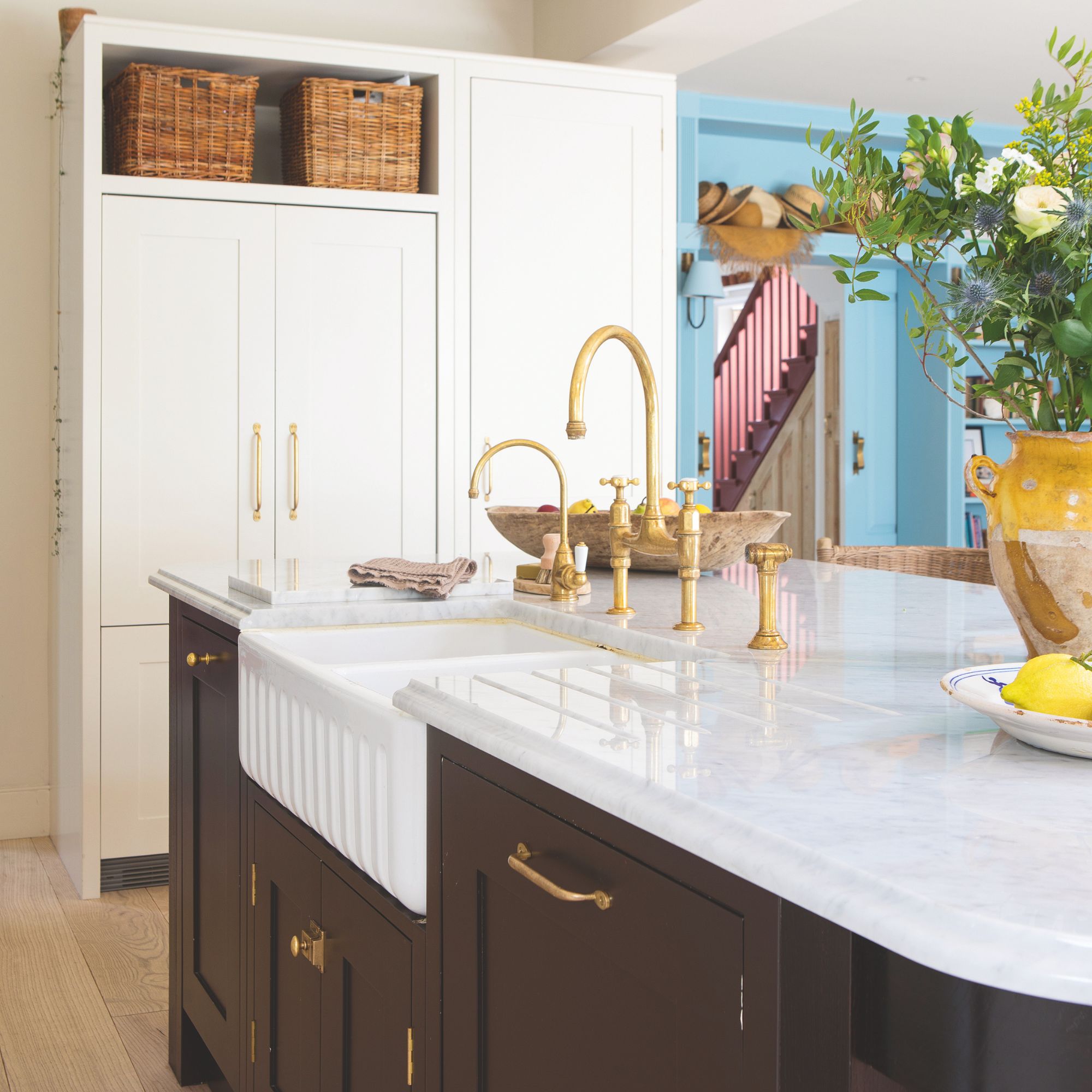 White painted kitchen with large white cupboards towards the back of the room, and a kitchen island in the middle with black cabinets and a white worktop