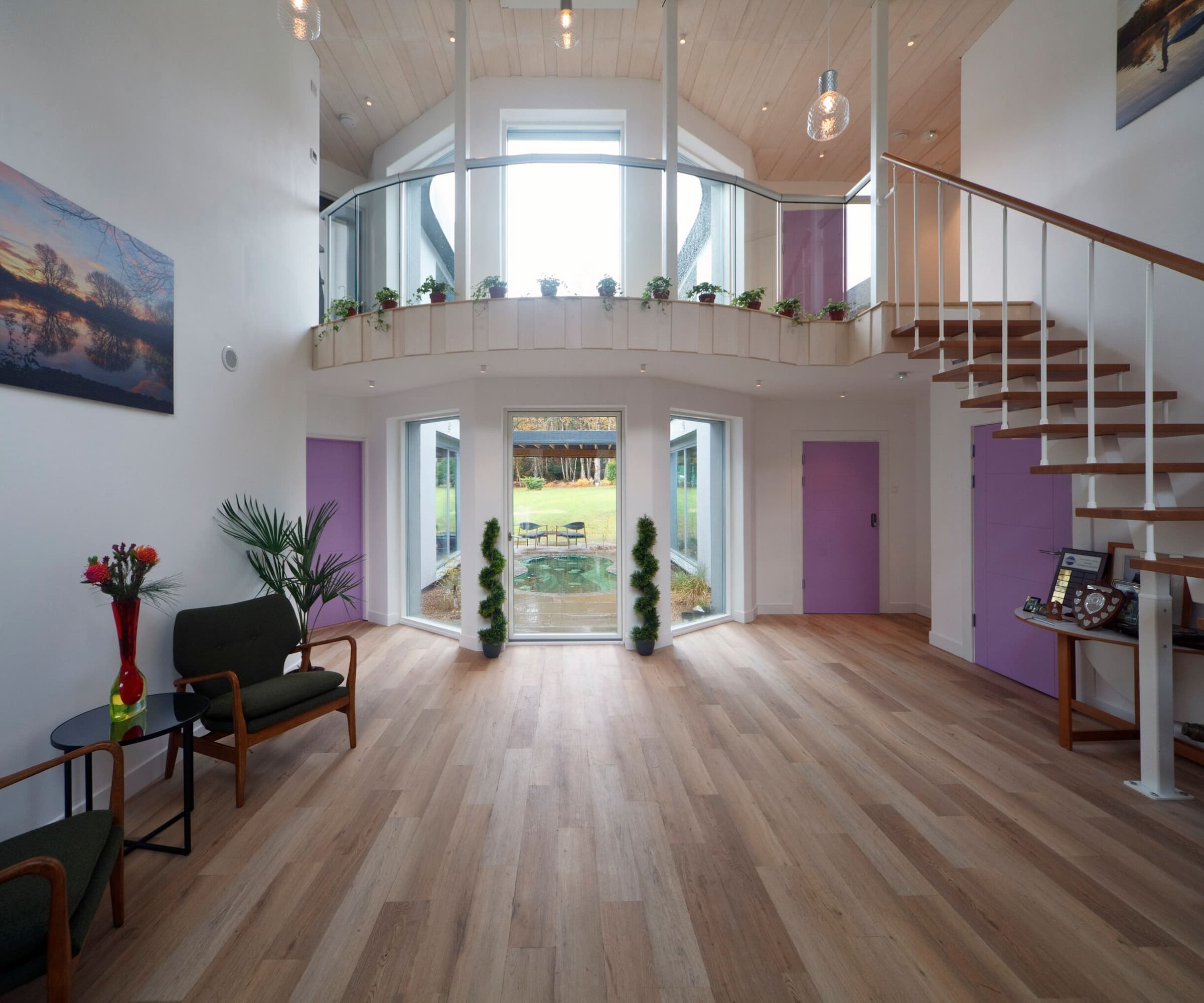 A hallway with a wooden floor and entrance with a staircase leading to a balcony