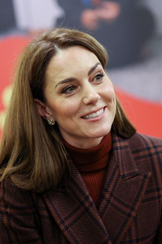 Princess Kate wearing a red turtleneck, maroon plaid coat smiling and looking up to the right