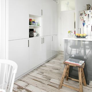 A wall of floor to ceiling white kitchen cabinets with a wooden floor and kitchen island