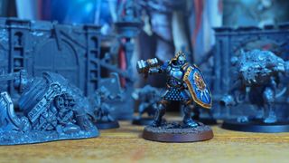 A painted Warhammer Age of Sigmar Stormcast Eternal model stands against Skaven miniatures from the Skaventide box set