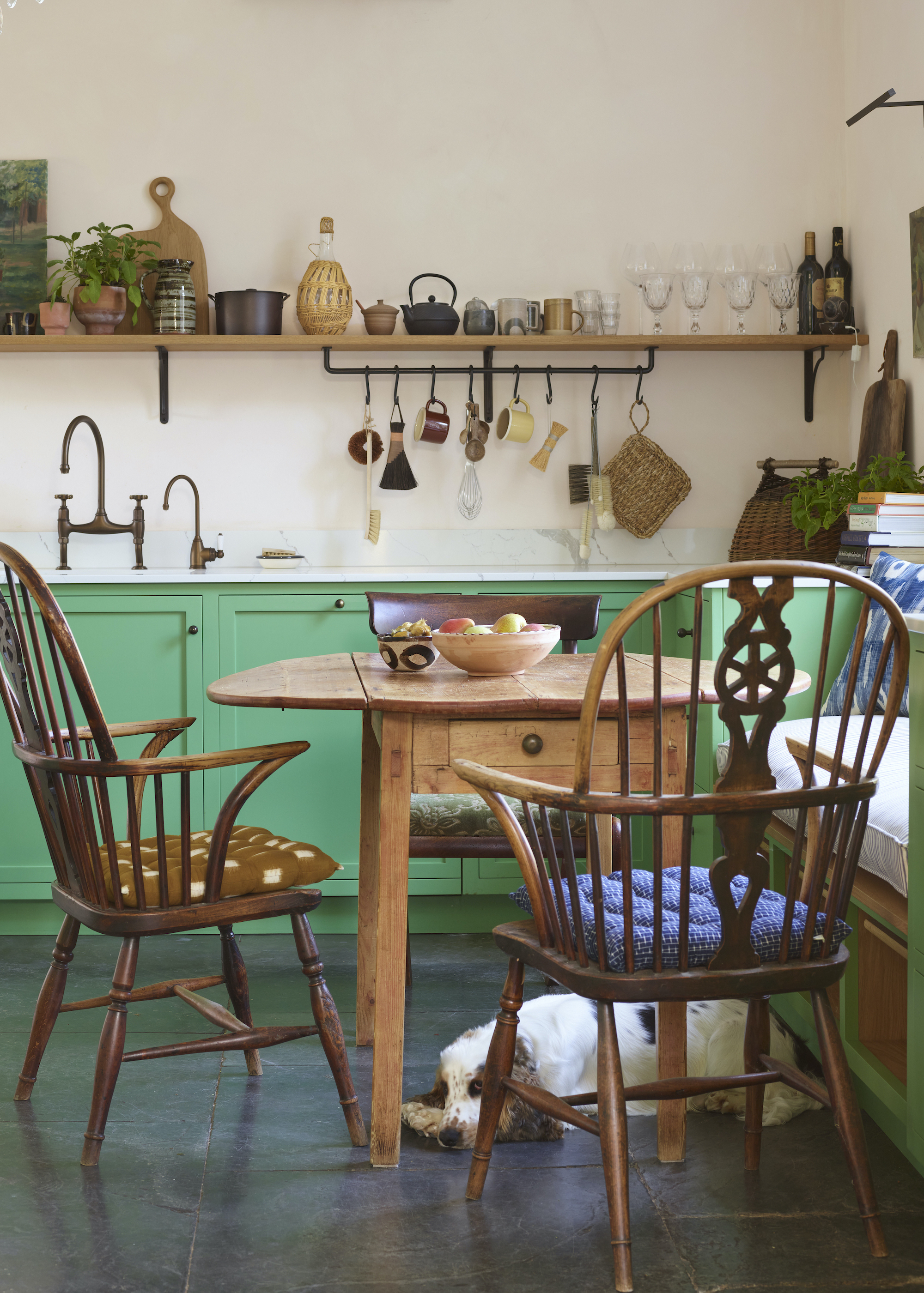 Green kitchen with small table and bench seat beside it. On the table is a bowl of fruit.