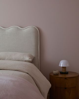 pink bedroom with wavy headboard, round timber side table with mushroom lamp