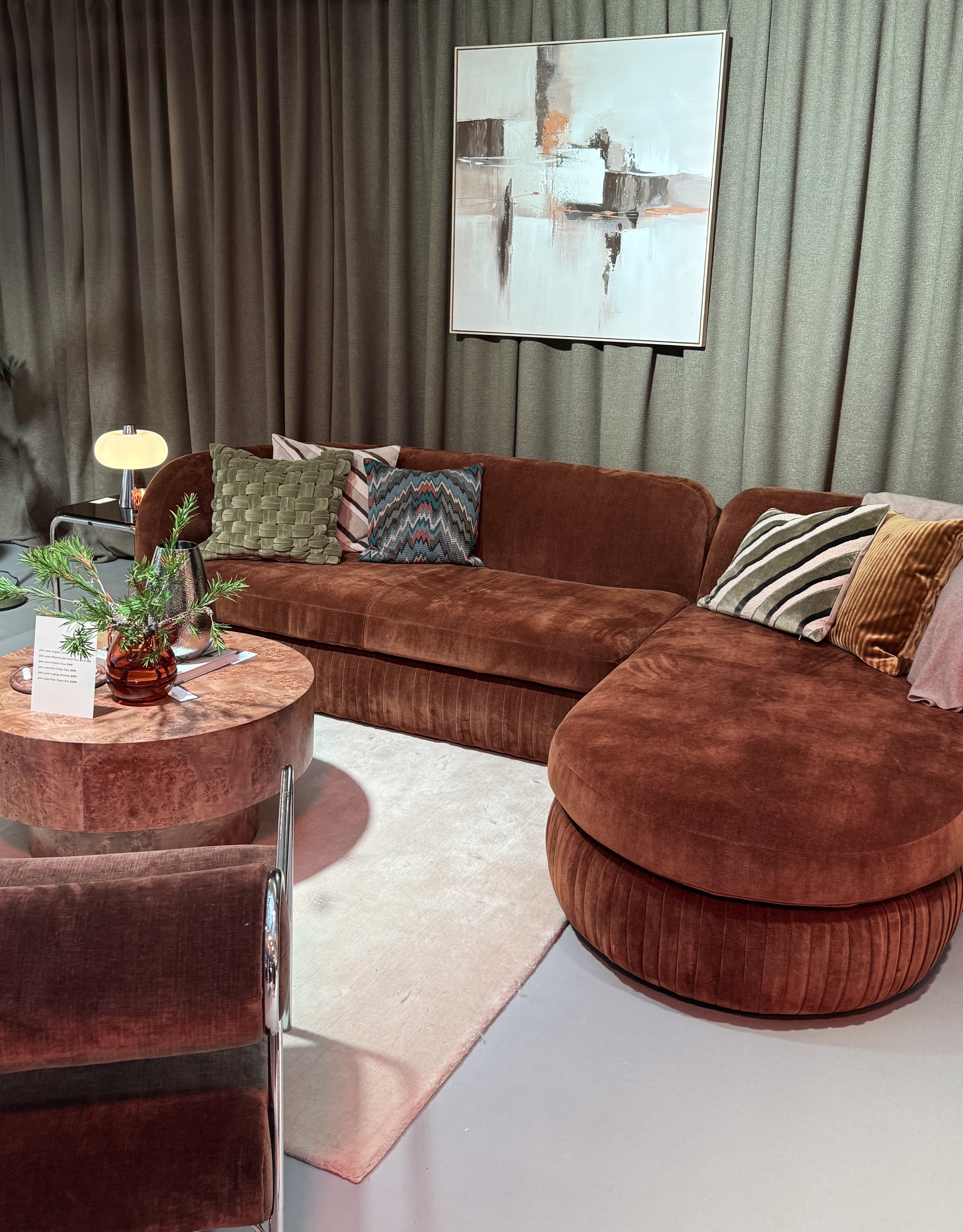 john lewis pleat sofa in a showroom with curtain wall and artwork, burl coffee table styled, beige rug, and brown and chrome armchair