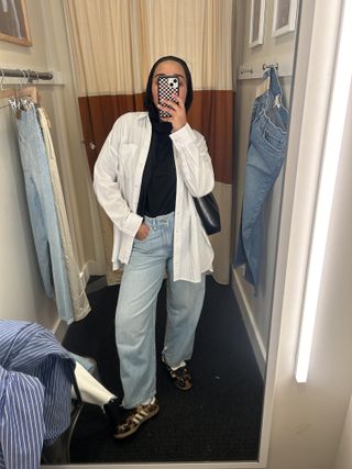 Yusra Siddiqui wearing button down, blue jeans, and sneakers in Madewell dressing room