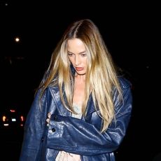 Margot Robbie wearing a navy leather coat, ruffled top, jeans, and satin ballet flats