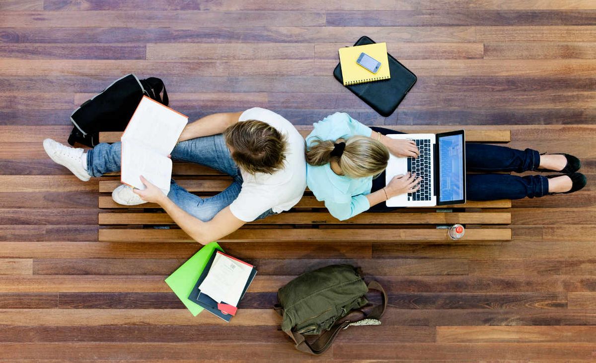 View from above of teenage students on wooden bench, studying with their laptop computers.