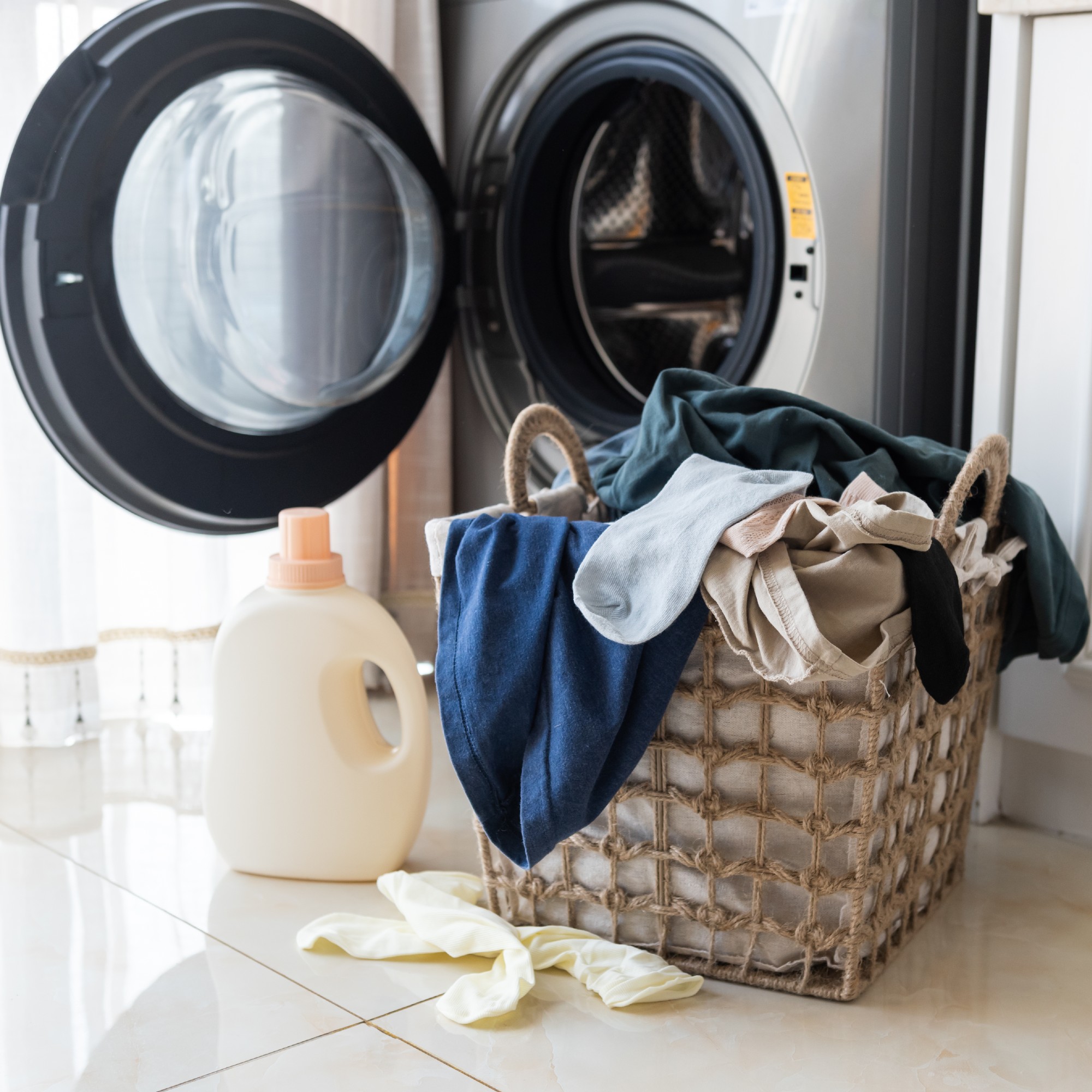 Laundry in a basket in front of a tumble dryer next to a bottle of fabric softener