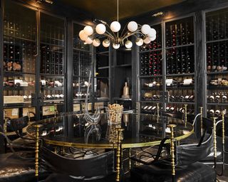 A wine cellar with black and glass cabinetry, brass fittings, a large mirrored table and chandelier