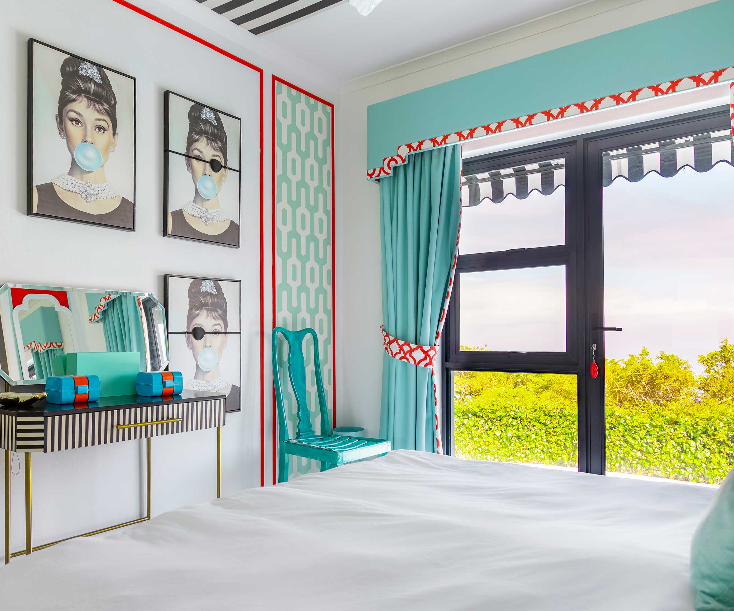 white bedroom with bright aqua blue curtains and pictures of Audrey Hepburn on the wall