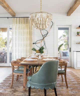 Large white dining room with beige scalloped rug, wooden dining table, low hanging pendant