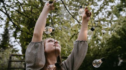 Smiling woman hanging lighting equipment in yard during dinner party