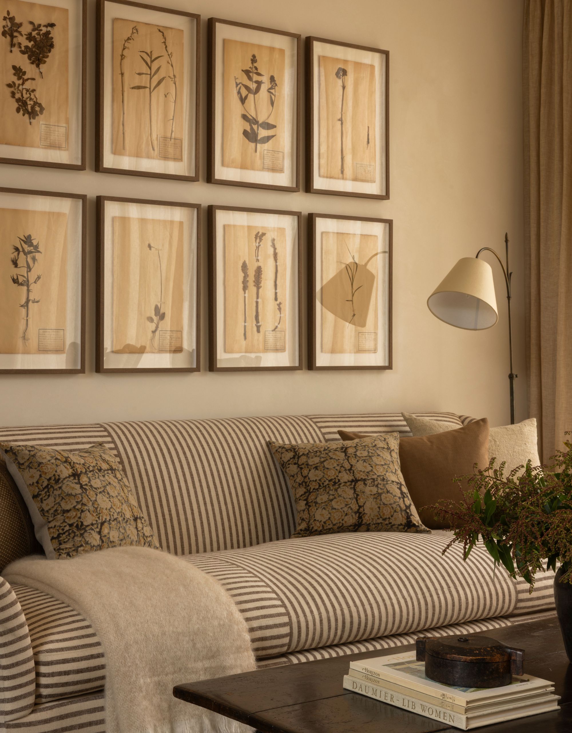 A modern neutral living room with a striped sofa in front of a wall of eight framed botanical prints with a black coffee table