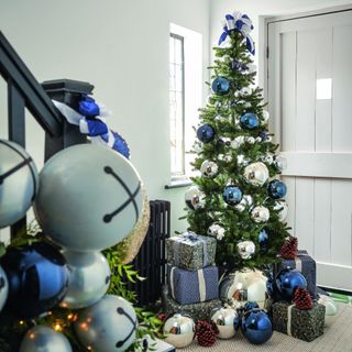 A hallway with a Christmas tree by the door decorated with glossy blue and silver baubles and a bow on top