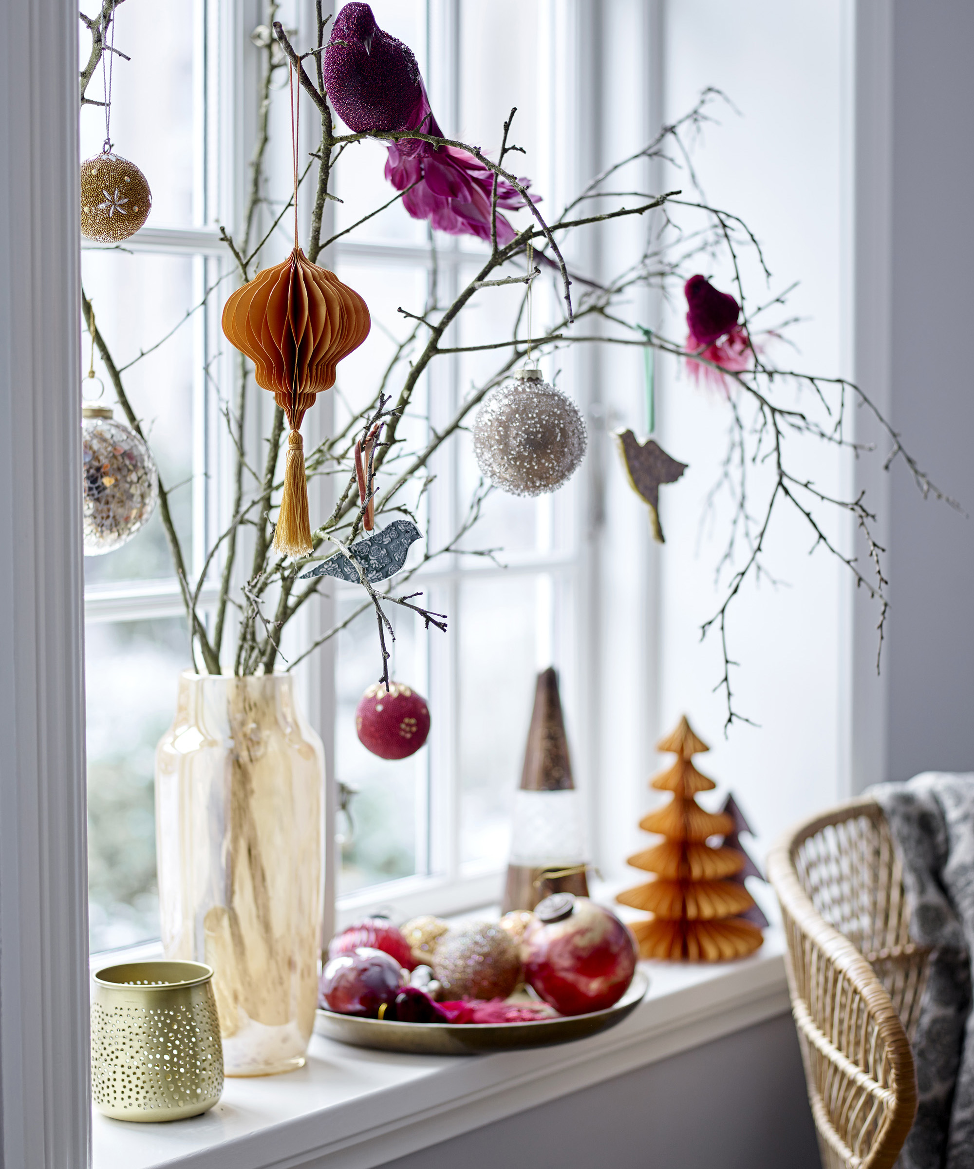 A living room with vase by window with branches and paper honeycomb decorations