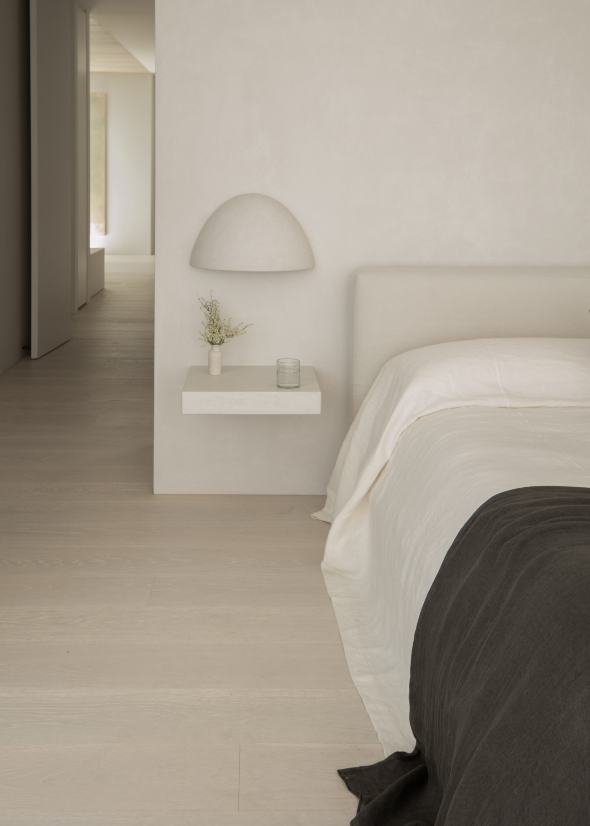A white bedroom with a floating bedside table and a wall sconce