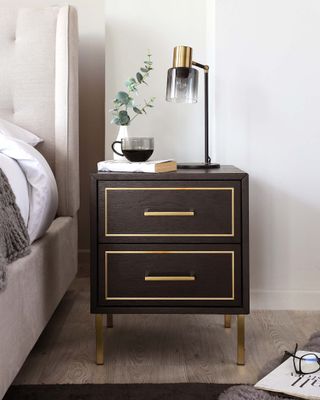 A walnut nightstand next to a bed, with a lamp on it