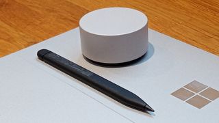 Microsoft Surface Dial review; a silver cylinder gadget with a black stylus pen on a silver laptop