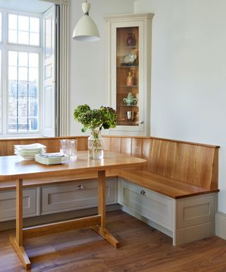 Traditional breakfast nook with bespoke wooden banquette seating, a matching dining table, soft grey cabinetry, and a glass-fronted corner display cabinet in a Georgian home.