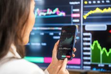 A businesswoman examines financial charts and graphs on her smartphone, utilizing modern technology for investment analysis amidst digital screens displaying stock data.