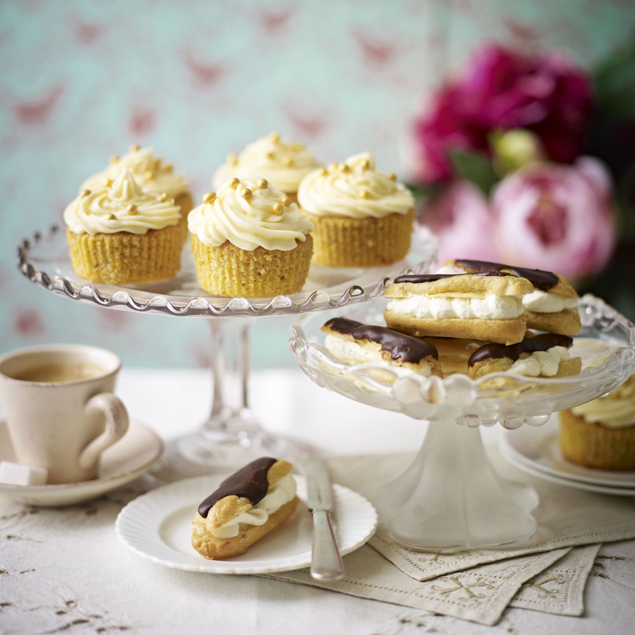 Chocolate and ginger cupcakes on a glass cake stand with eclairs and flowers