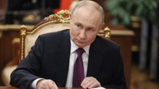 Vladimir Putin on a gold chair in a suit, signing a document