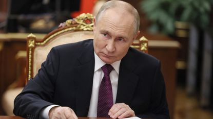 Vladimir Putin on a gold chair in a suit, signing a document