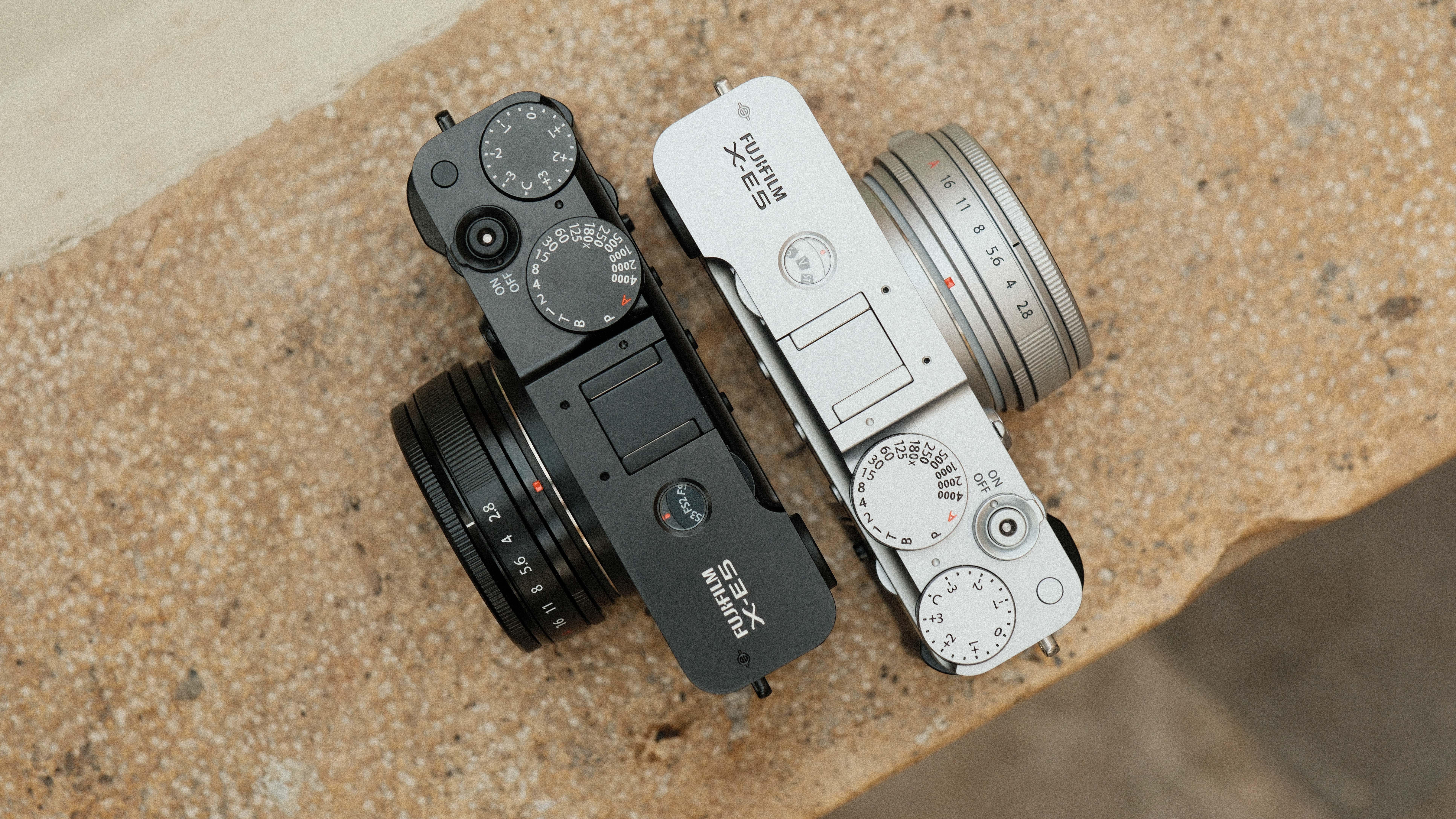 Two Fujifilm X-E5 cameras in black and silver next to one another on a stone wall