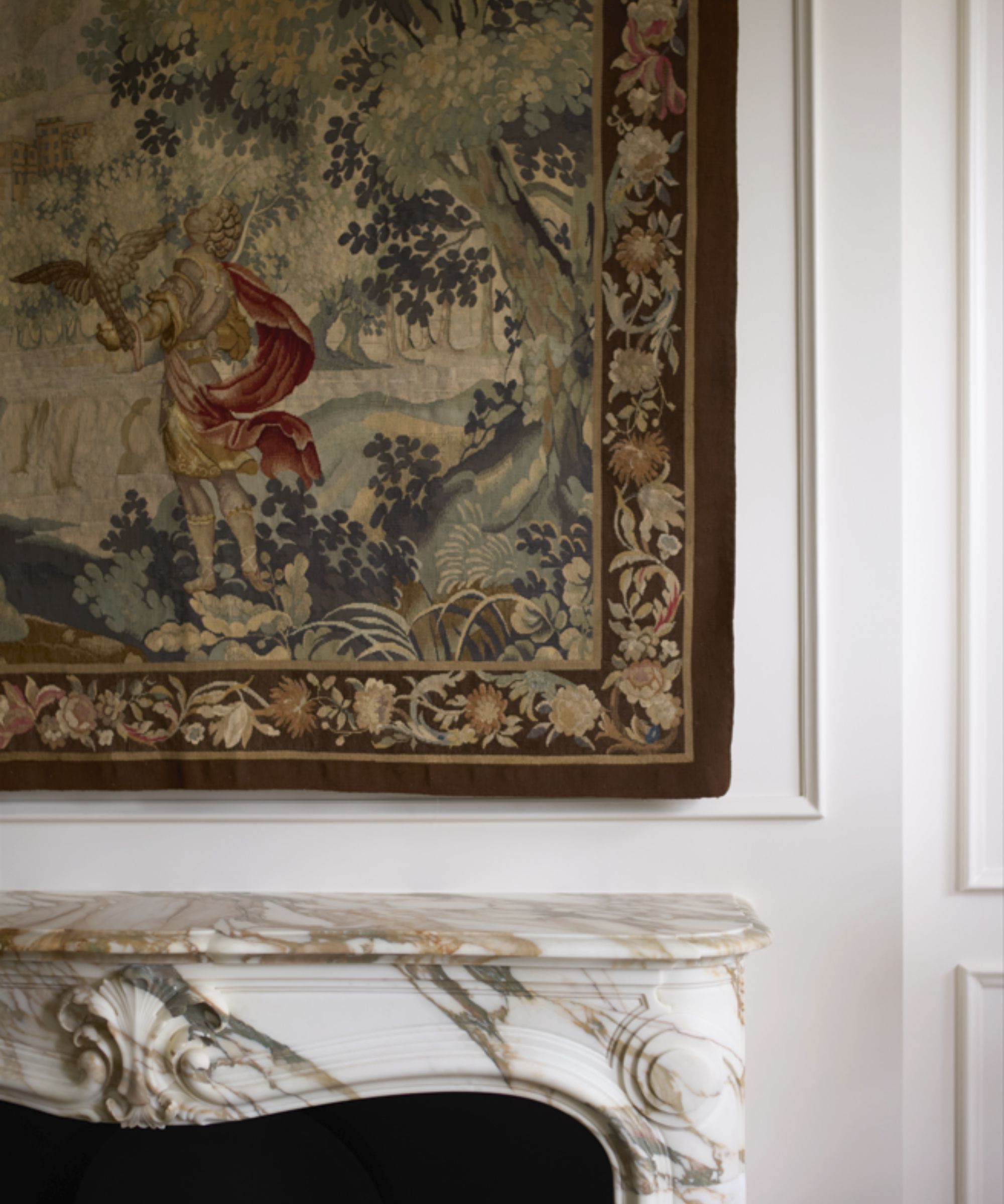 Close up of patterned tapestry hanging above a marble fireplace