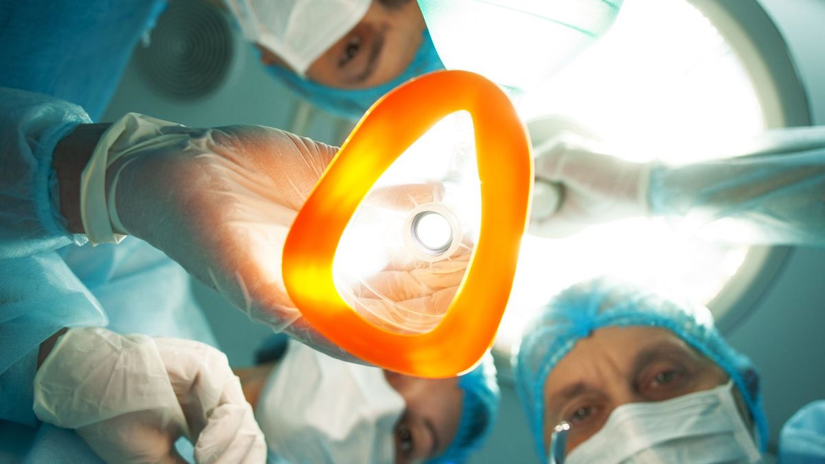 team of masked surgeons gathered around a bed and lowering an oxygen mask onto the viewer