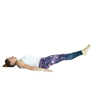 Woman in exercise clothes lying down on floor with arms by her sides, legs pointed up and out with toes pointed