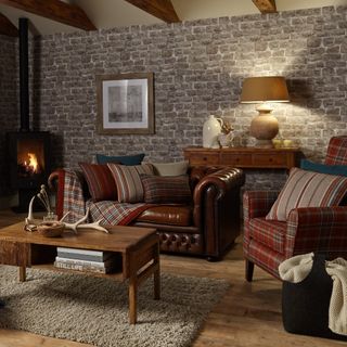 A living room with a brown leather sofa with striped and checked cushions and throws with a console table behind it and a turned on table lamp on top of it