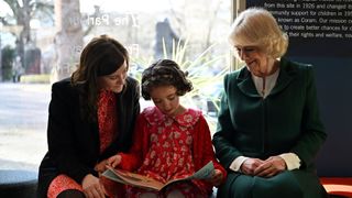 Queen Camilla reading with a child and a charity worker