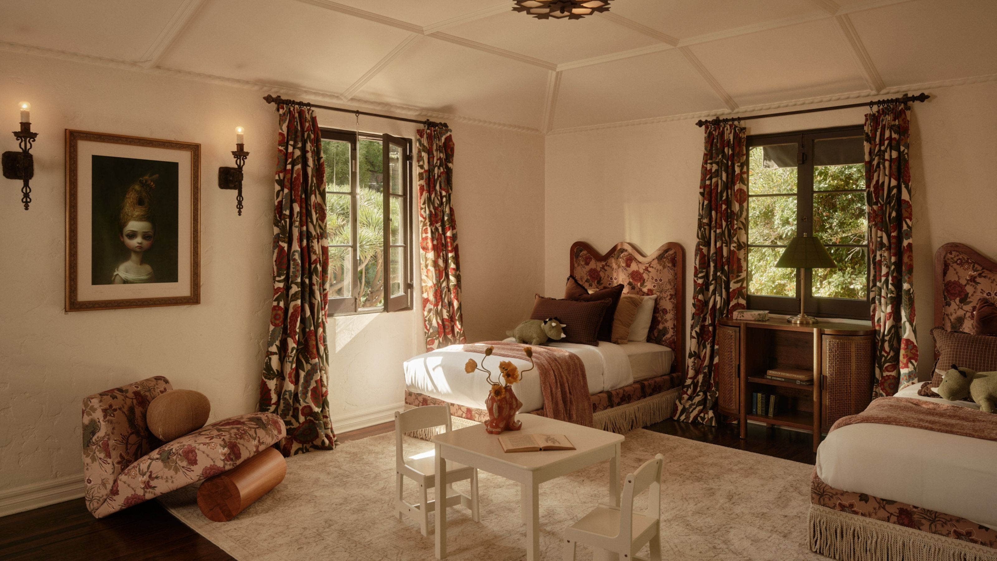 Image of a large bedroom with two twin beds on either side of a window. The beds have sculptural, patterned headboards with white bedding and dark brown pillows. The curtains and accent chair match.