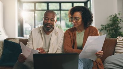 A couple look over paperwork together on their living room sofa.