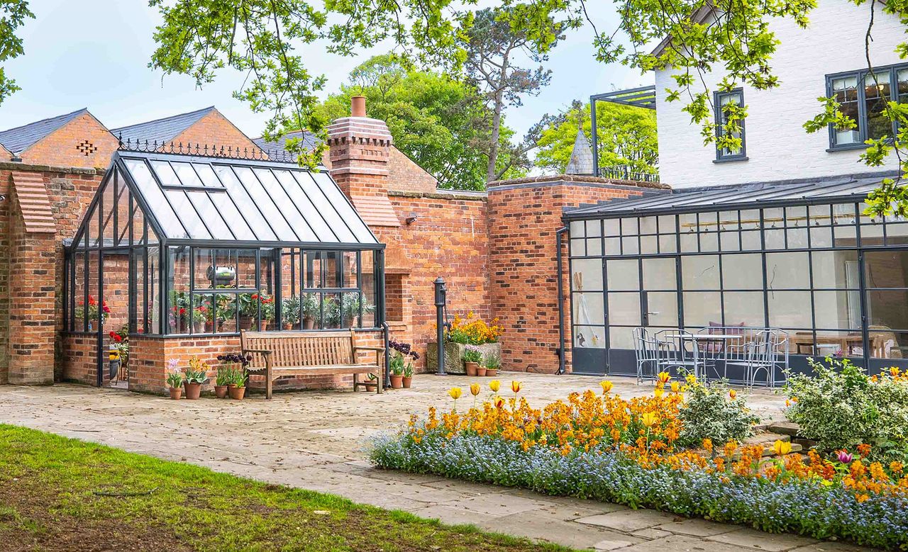 greenhouse against a wall in a garden alongside a house with a glazed extension hartley botanic