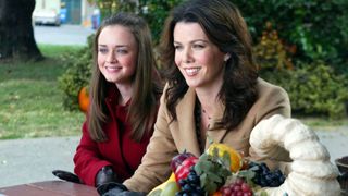 Rory and Lorelai Gilmore sit at a picnic bench smiling