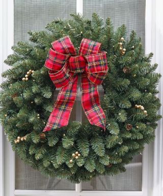 A Christmas wreath with a red and green bow on a front door.