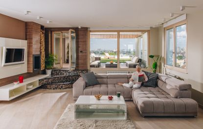 A woman sitting on her couch, reading a magazine in a luxury condo. 