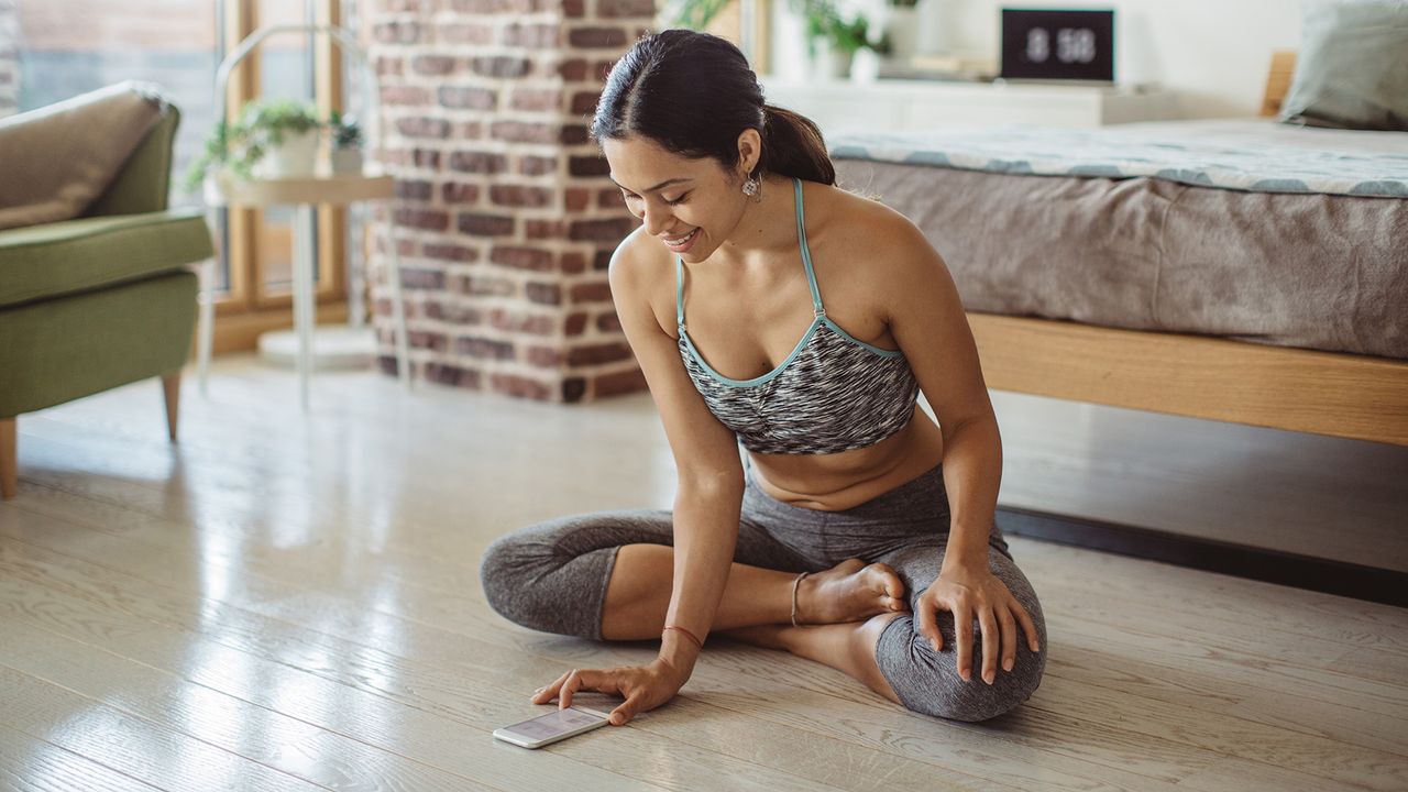 A woman in workout wear looks at a health and fitness app on her mobile phone