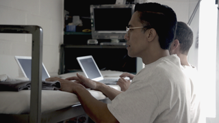 Two people work on laptops on a bed.