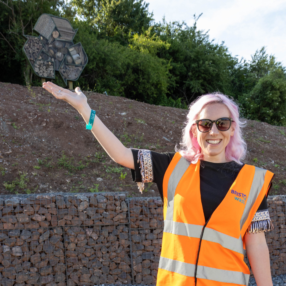 Hannah Deas wearing an orange safety vest and putting her hand under a recycling symbol in the background