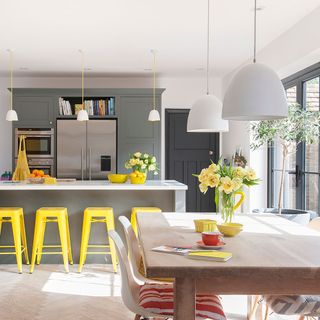 kitchen area with grey kitchen units and white ceiling lamps and white countertop and yellow table