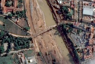 a waterway with a lot of dirt in it, with a bridge overhead. buildings surround the banks