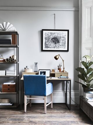 Neptune Carter desk, Brompton desk lamp in Antique Brass , City plan print framed on the gray wall, and wooden floor underfoot, with stylish wooden furniture and desk and blue desk chair