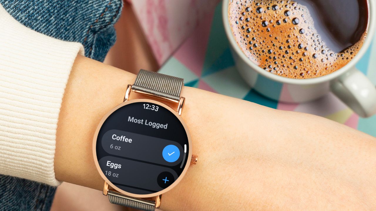 A Wear OS smartwatch on a wrist by a cup of coffee