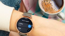 A Wear OS smartwatch on a wrist by a cup of coffee