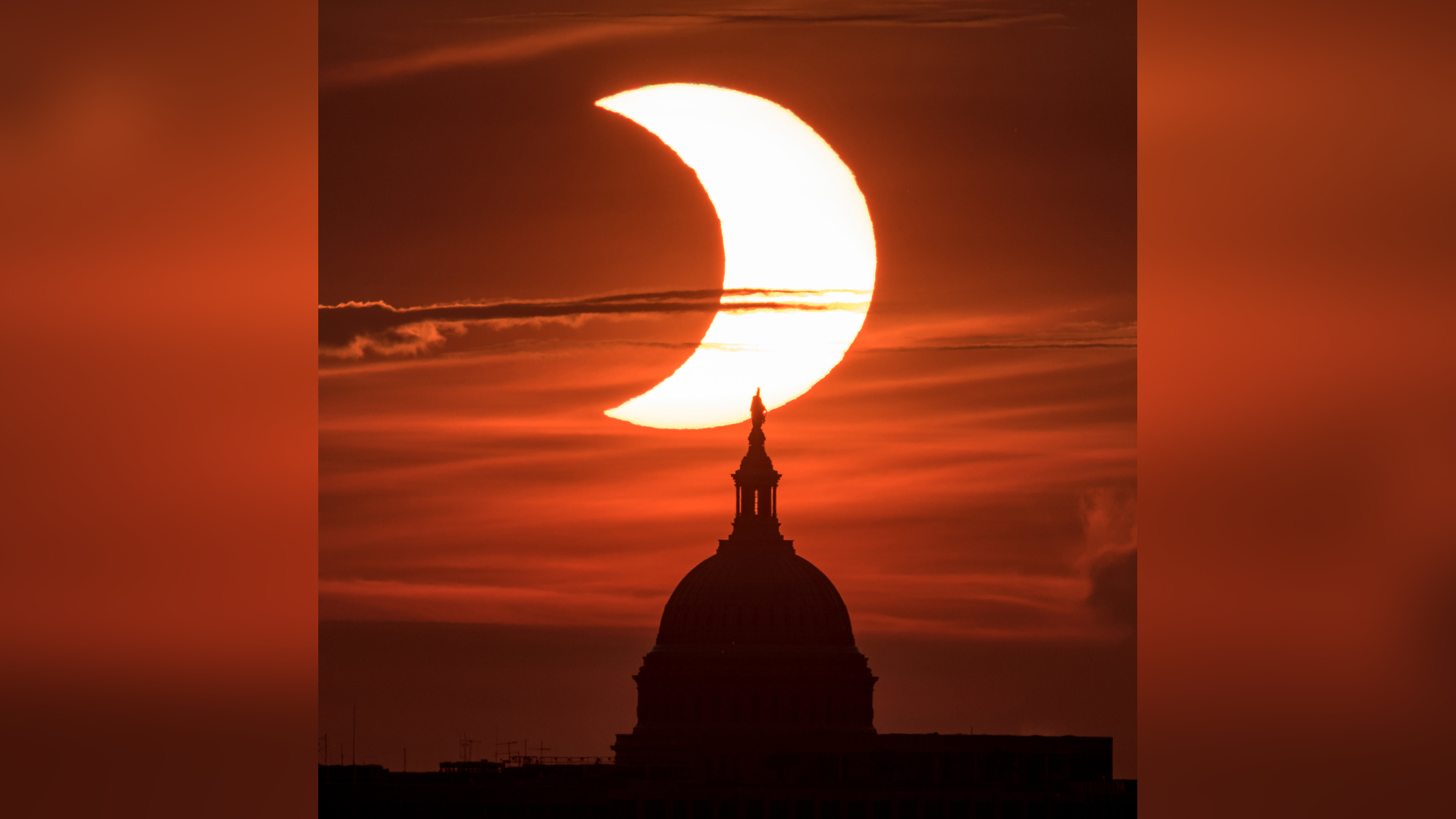 A partial solar eclipse is seen as the sun rises behind the United States Capitol Building, Thursday, June 10, 2021, as seen from Arlington, Virginia.