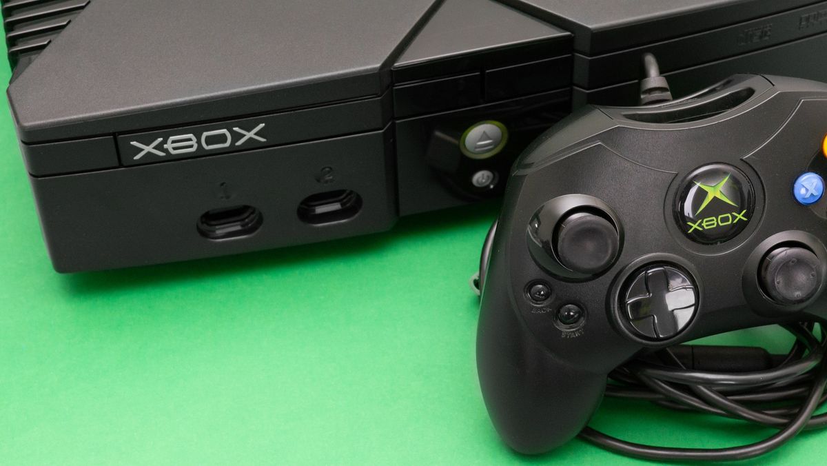 Microsoft’s original Xbox console powered on, on a green surface, and with a Controller S sitting in-front.