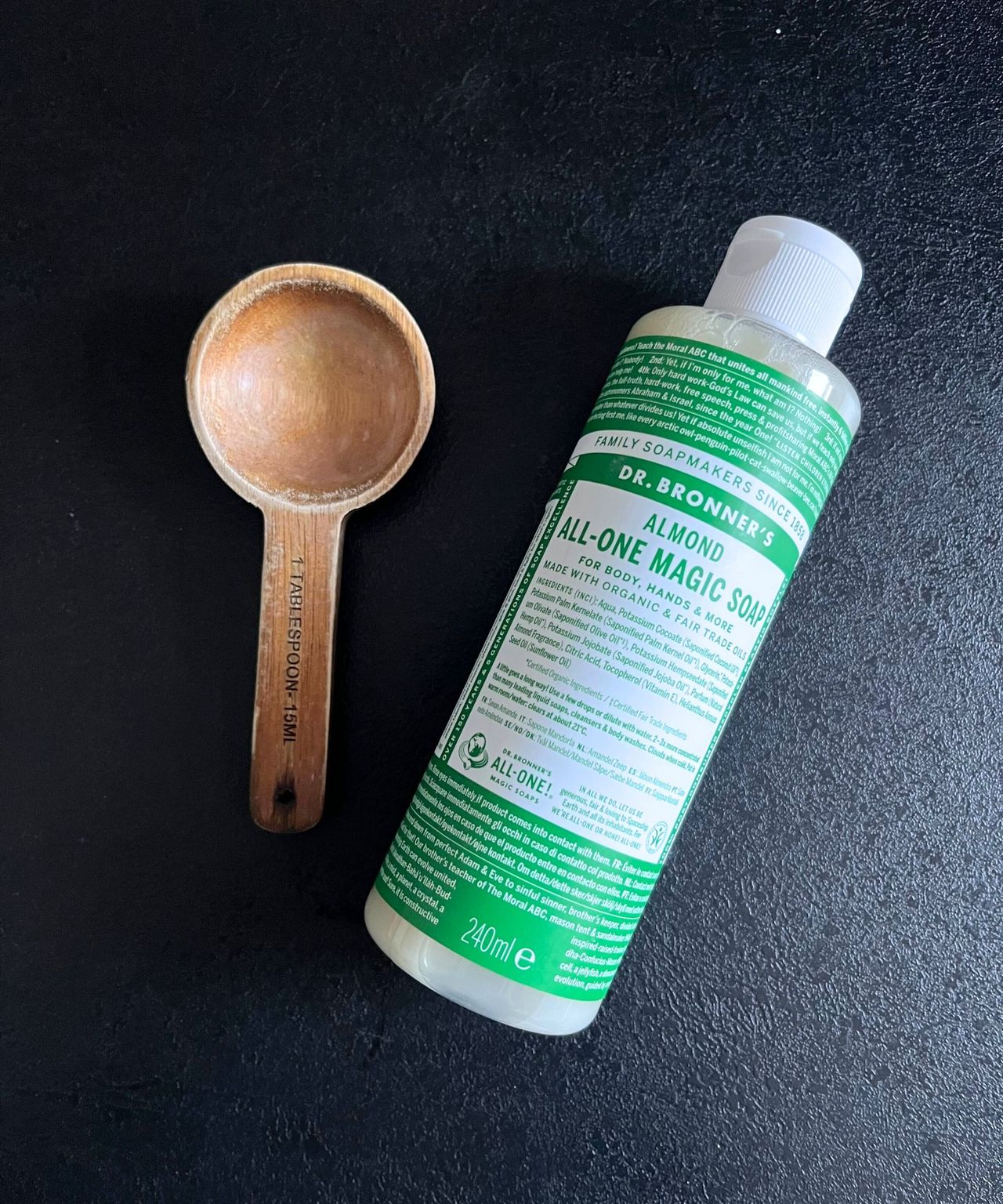 A wooden tablespoon measure next to a green bottle of Castile soap